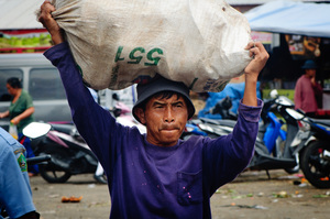 A man carries a heavy load through a rural market in Bali, Indonesia.
