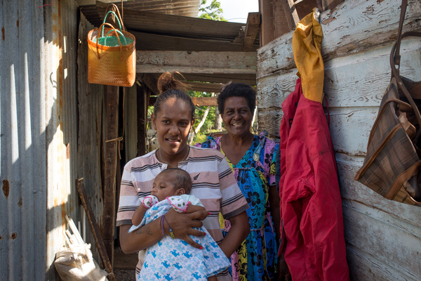 Wilma holds her baby, Francois, in the middle of their family home on Ifira island. It is still in need of major renovations three months after cyclone Pam caused extensive damage. Her mother smiles in the background.
