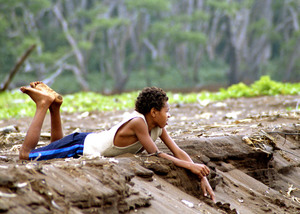 A young boy lounges on the black sand beach near the mouth of the Silver
river, waiting for his mates to return from diving on the reef nearby.

