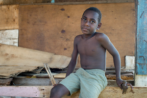 A boy with a hammer sits in a half-finished house.
