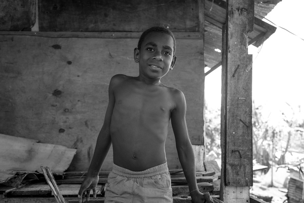 A boy with a hammer sits in a half-finished house.
