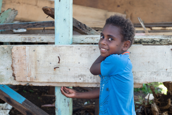 A girl stands beside a half-constructed house made from salvaged materials.
