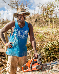 A young woman smiles in wreckage the day after cyclone Pam destroyed her mother's handicrafts stall at Port Vila's seafront. In the background is a sign exhorting people to keep Port Vila clean.
