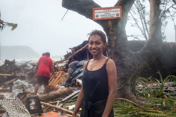 A young woman smiles in wreckage the day after cyclone Pam destroyed her mother's handicrafts stall at Port Vila's seafront. In the background is a sign exhorting people to keep Port Vila clean.
